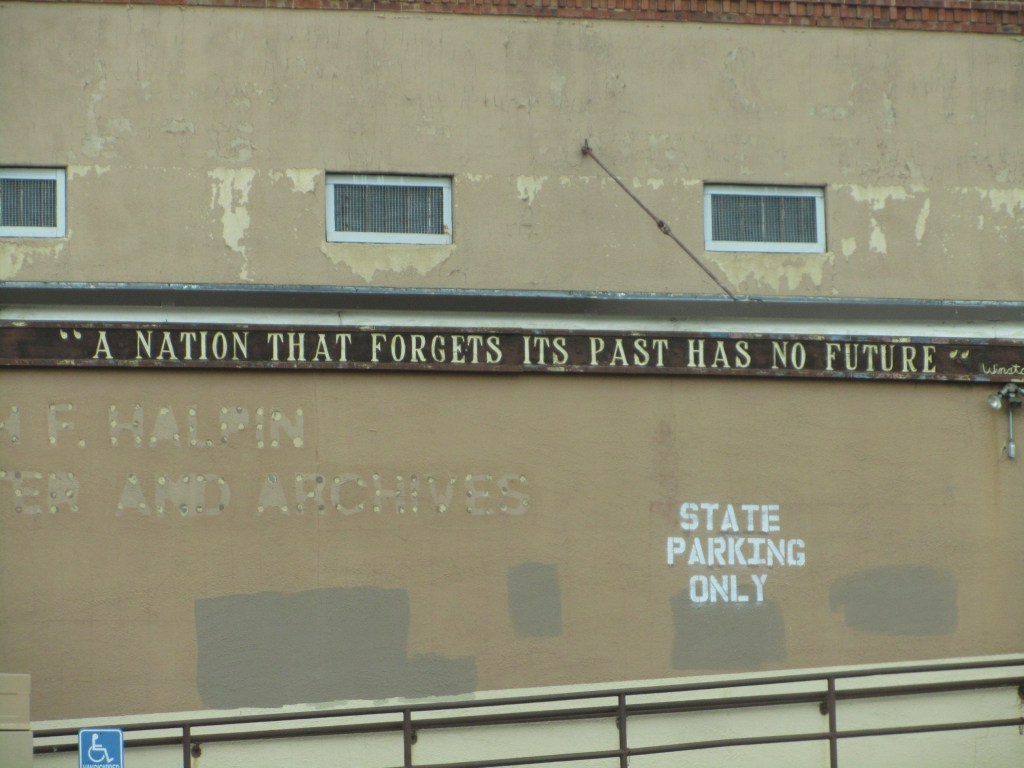 "A nation that forgets its past has no future" quote on a wall, with faded text indicating "J. F. Halpin Center and Archives" and a sign that says "STATE PARKING ONLY".