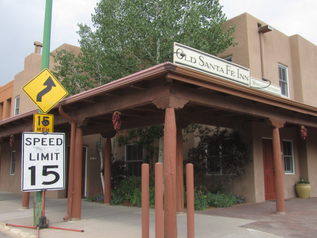 Exterior view of Old Santa Fe Inn with a speed limit sign and a directional curve sign in the foreground.