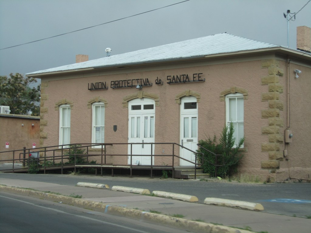 Facade of the Union Protectiva de Santa Fe building, featuring a ramp and cream-colored walls with a sign above the entrance.