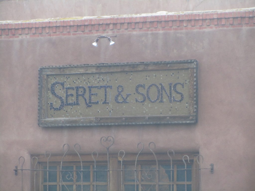 Sign for Seret & Sons featuring decorative tiles, mounted on a textured wall.