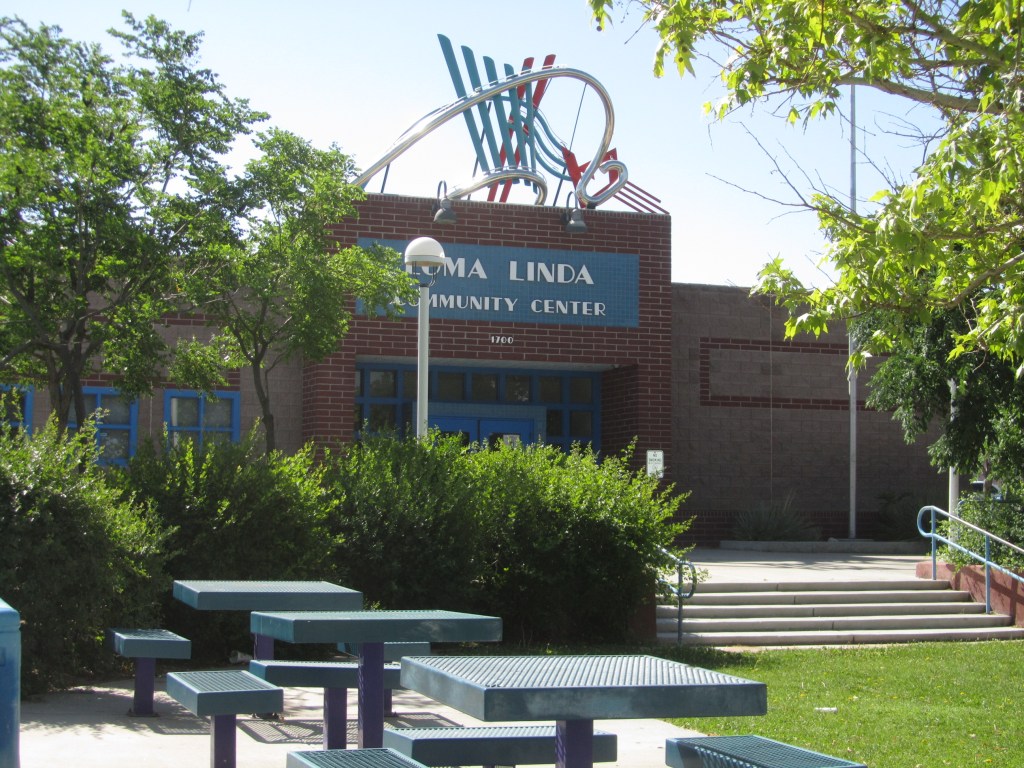 Exterior view of the Loma Linda Community Center with decorative features on the rooftop, surrounded by trees and benches.