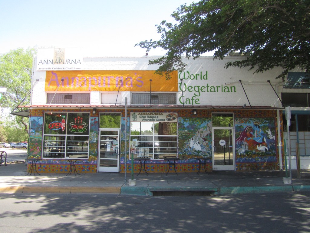 Exterior view of Annapurna's World Vegetarian Cafe, featuring colorful murals and an open sign, with outdoor seating available.