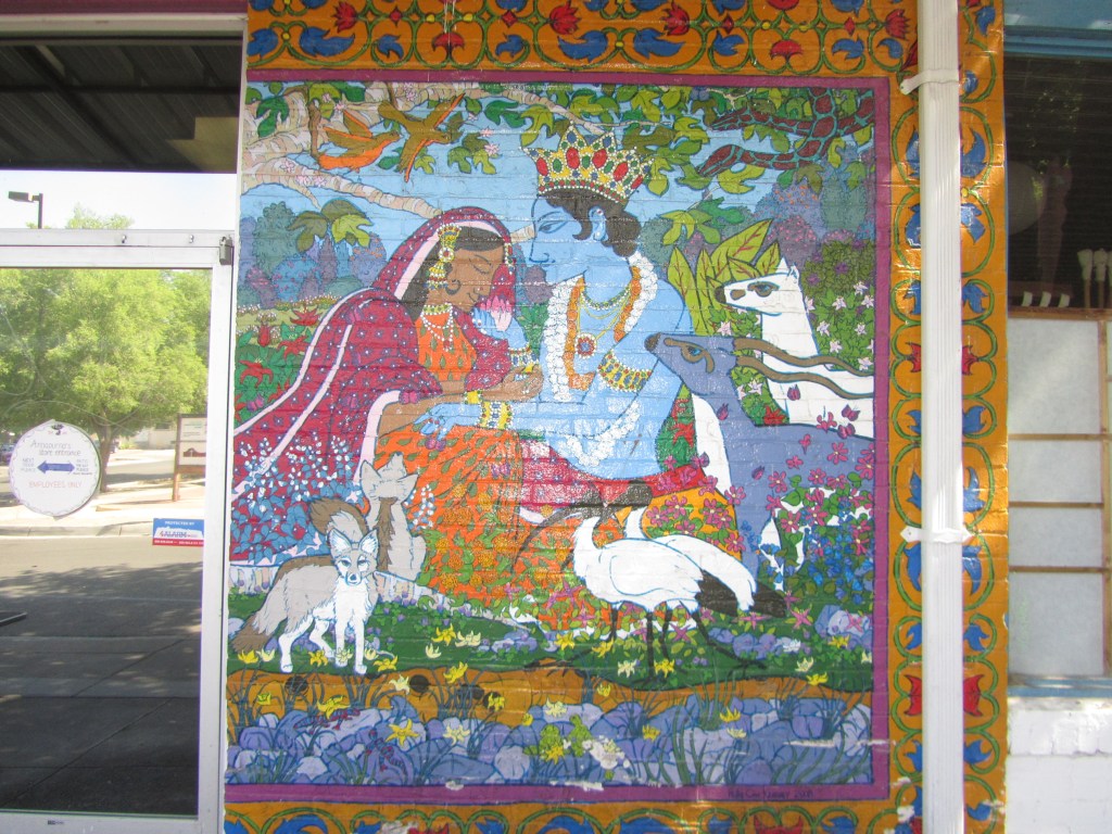 A vibrant mural depicting a scene with deities, featuring a blue-skinned figure and a woman in traditional attire surrounded by animals and nature.